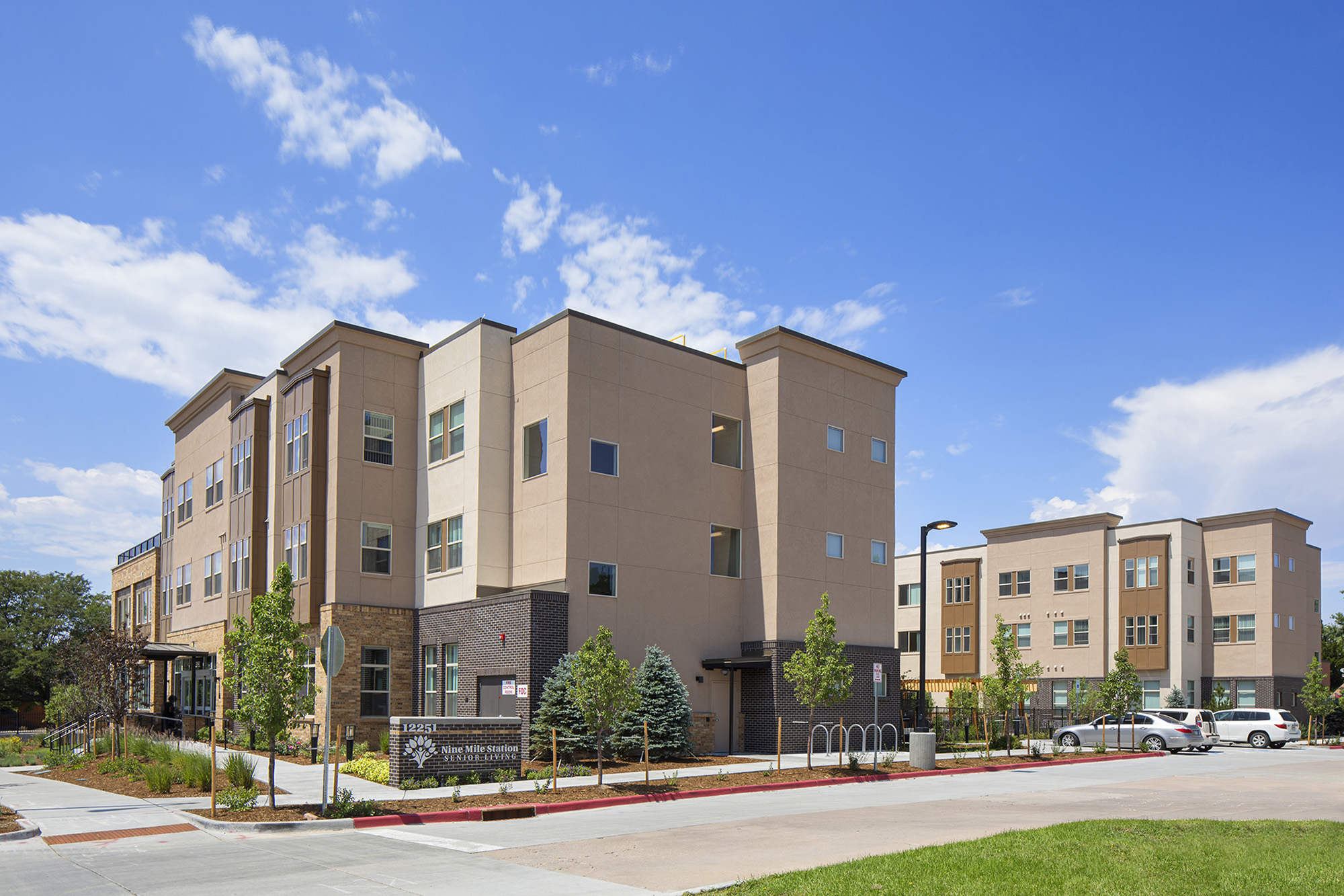 Corner view of 3 storey apartments with signage, trees, sidewalk