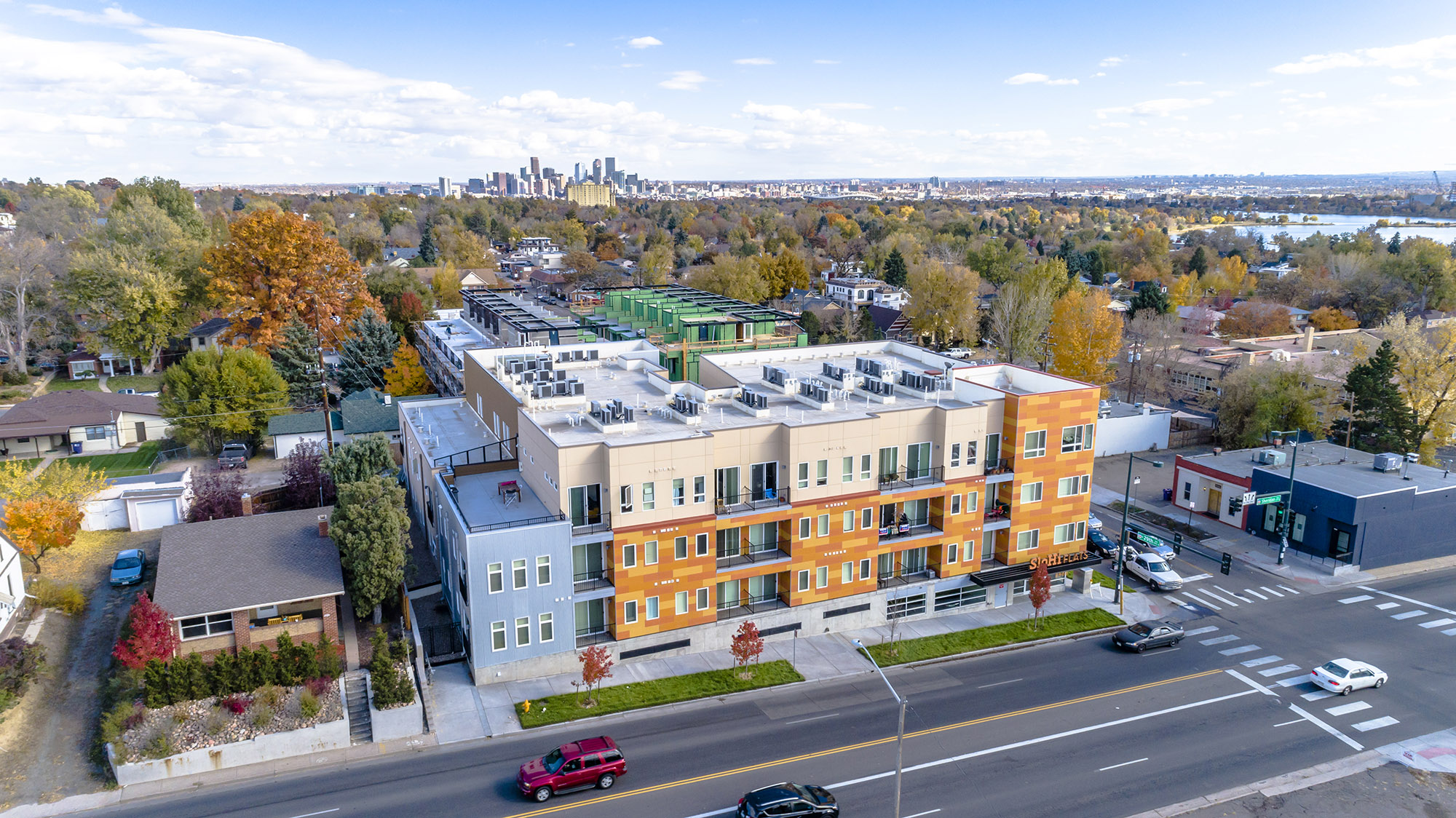 bird's eye view of 4 storey building with sloan's lake and downtown skyline in background