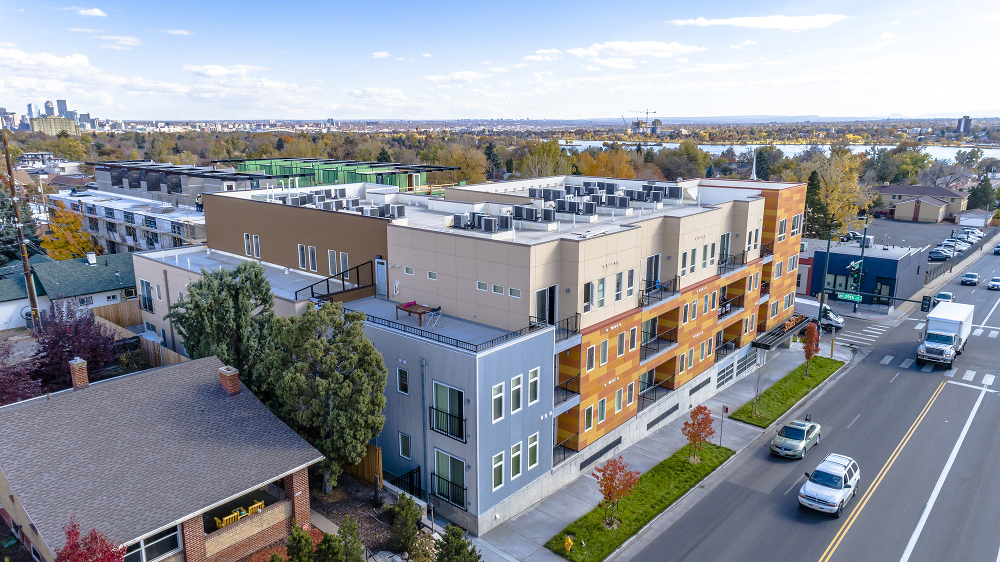 bird's eye view of 4 storey building with sloan's lake and downtown skyline in background