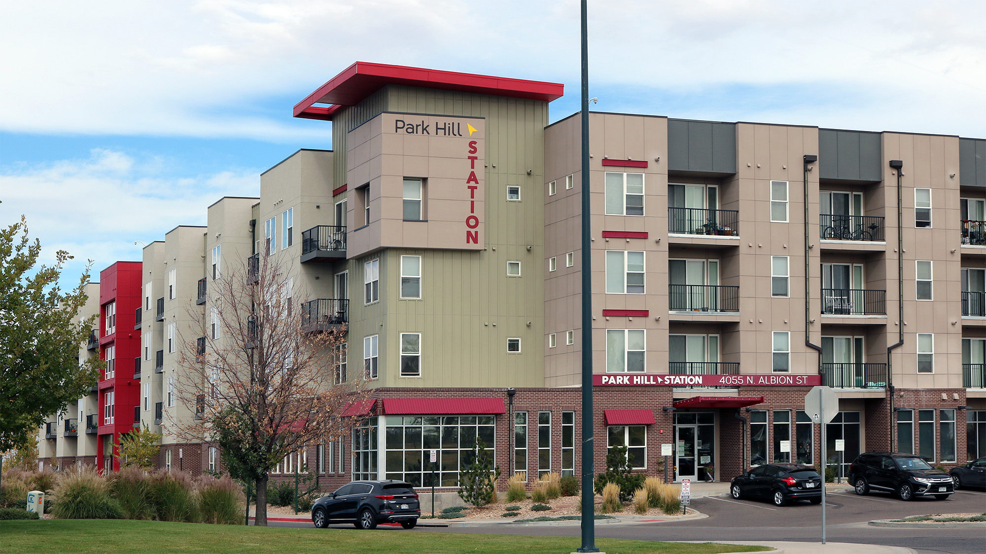 Photo of exterior corner of 4 storey apartment building with signage and red awnings Parkhill Station